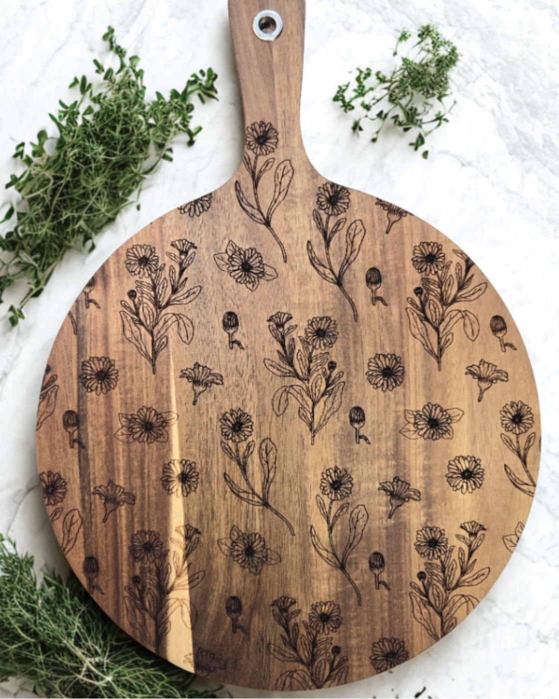 Wooden cutting board with floral patterns on a white surface with green herbs.